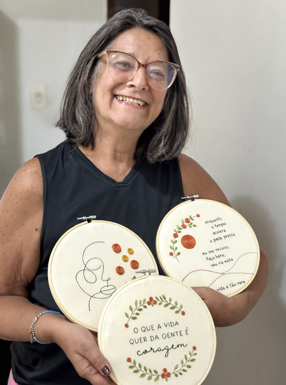 Vitória, a Vi, segurando três bordados feitos à mão